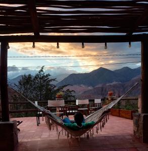 a person laying in a hammock on a porch with a view at Hostal de Altura in Tilcara