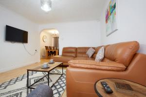 ein Wohnzimmer mit einem braunen Ledersofa und einem TV in der Unterkunft HAVEN HOUSE DETACHED Residence in Headingley