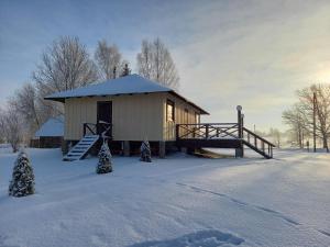 um pequeno edifício na neve com árvores de Natal em Rūnēnu zāļu namiņš em Vidzeme