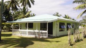 a green house with a white porch and palm trees at Flame Cottage in Rarotonga