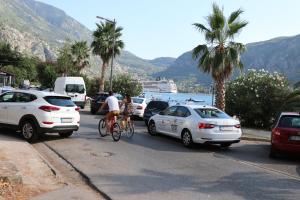 two people riding bikes and cars on a street with palm trees at Apartment Sandrita in Kotor