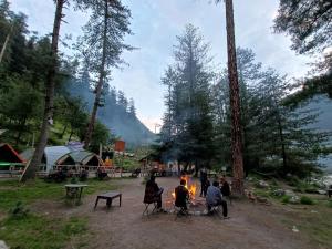 Un groupe de personnes assises autour d'un feu de camp dans l'établissement Himtrek Riverside Camps, Kasol, à Kasol