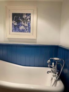 a bath tub in a bathroom with a painting on the wall at Baker's Cottage in Castle Combe