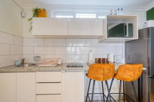 a kitchen with white cabinets and two bar stools at Hampton Collection - Trendy 2 Sleeper Apartment with Pool in Durban