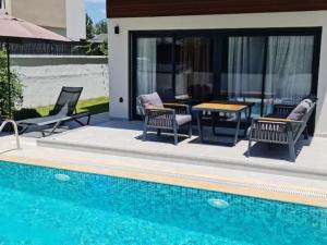 a pool with chairs and a table next to a house at Room in Villa - Cheerfull Brand New 4 Bedrooms Villa with Pool in Fethiye