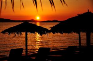 Sunday Luxury Suites في أغيا أنا ناكسوس: غروب الشمس على الشاطئ مع الكراسي والمظلات