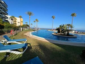 una piscina con 2 tumbonas y el océano en MI CAPRICHO, Beach Front Apartment P.14 3ºB, en Mijas Costa