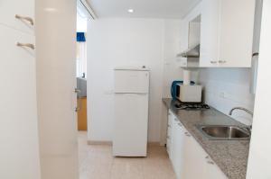 a white kitchen with a sink and a refrigerator at Apartamentos Siglo XXI - Sant Joan in Sant Feliu de Guíxols