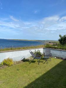 a couple of chairs sitting on a lawn next to the water at Four waves in Thurso