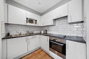 una cucina con armadi bianchi, lavandino e piano cottura di Marble DELUXE - City Centre Apt- Parking & Wifi a Maidstone