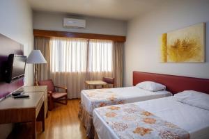 Cette chambre comprend deux lits, un bureau et une télévision. dans l'établissement Hotel Nacional Inn Belo Horizonte, à Belo Horizonte