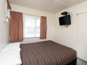 a bedroom with a bed and a flat screen tv at Avon Motel in Hawera