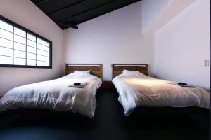 2 łóżka w pokoju z białymi ścianami i oknem w obiekcie Shibashi Umeyacho w mieście Kioto