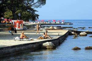 grupa ludzi siedzących na plaży blisko wody w obiekcie Apartments with a parking space Umag - 6959 w mieście Umag
