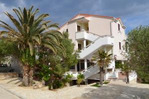 a white building with palm trees in front of it at Apartments and rooms by the sea Jakisnica, Pag - 4160 in Lun