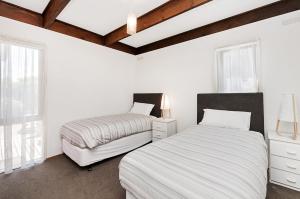 2 Betten in einem Zimmer mit weißen Wänden und Fenstern in der Unterkunft Swimmers Rest in Port Fairy