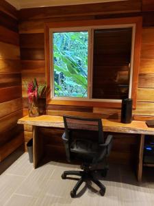 einen Schreibtisch mit einem Stuhl vor einem Fenster in der Unterkunft Cabina Harlequin at Margarita Hills Farm in Cocles