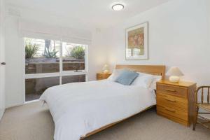 a white bedroom with a bed and a window at Cosy Back Beach Hideaway with Fire Pit. in Portsea