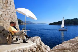 un hombre sentado en una mesa con un velero en el agua en Apartments by the sea Dubrovnik - 4698, en Dubrovnik