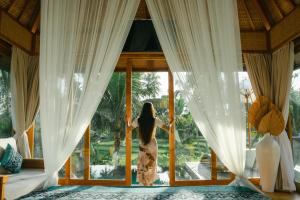 a woman standing in a bedroom looking out the window at Kappa Senses Ubud in Ubud