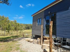 ein schwarzes kleines Haus mit Stühlen und einer Veranda in der Unterkunft Tiny Home - Bluebird in Hartley