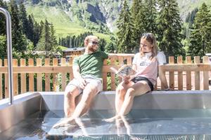 un homme et une femme assis sur un banc dans une piscine dans l'établissement Berghaus Schröcken - Hotel Apartments Spa, à Schröcken