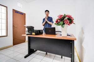 Ein Mann steht an einem Schreibtisch mit einer Blumenvase. in der Unterkunft OYO 91546 Dewi Sudirman Homestay in Bandung