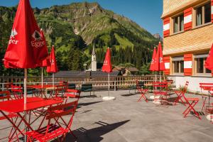 um grupo de mesas e cadeiras vermelhas com uma montanha em Berghaus Schröcken - Hotel Apartments Spa em Schröcken
