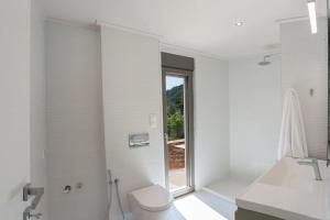 a white bathroom with a toilet and a window at Eucalyptus -- Agios Ioannis Beachfront Apartment in Lefkada Town