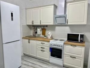 La cuisine est équipée de placards blancs et d'un réfrigérateur blanc. dans l'établissement Уютная квартира ЖК Сказочный мир город Астана, à Astana