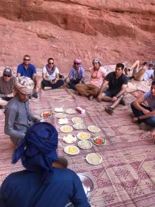 un grupo de personas sentadas en el suelo comiendo comida en Bedouins life camp, en Áqaba