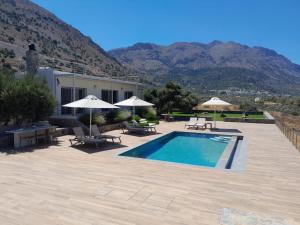 a swimming pool with chairs and umbrellas and a house at Villa Of the Hill with Heated Pool, BBQ & Kids Playground in Kavoúsion +40 photos