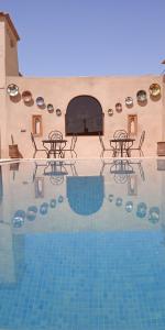 a swimming pool with tables and chairs in front of a building at RIAD dar POUBLANC in Merzouga