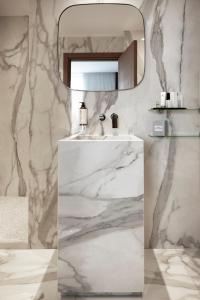 W wyłożonej białym marmurem łazience znajduje się umywalka i lustro. w obiekcie Howard sur Seine - Asnieres Paris La Defense w mieście Asnières-sur-Seine
