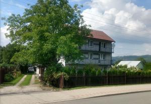 a house with a tree in front of a fence at Pokoje Rożnów in Rożnów