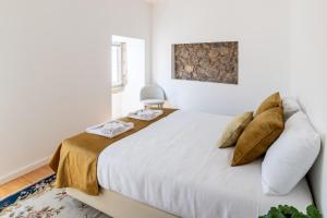 a white bedroom with a large white bed with gold pillows at Beautiful House in Miranda do Corvo