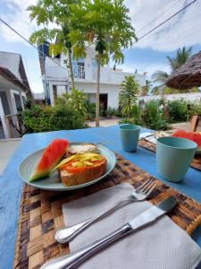 een bord eten op een tafel met een broodje en watermeloen bij Karibu House in Paje