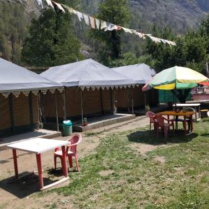 un grupo de mesas y sillas con sombrillas en una tienda de campaña en Snow View Himalayan Adventure, en Kasol