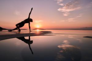 伊羅達的住宿－Elounda Gulf Villas by Sandglass，日落时在海滩上做瑜伽姿势的女人
