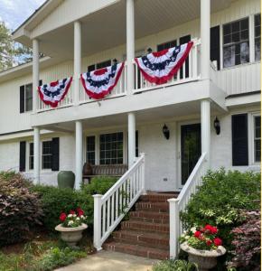 Uma casa branca com bandeiras americanas no alpendre. em The Birdnest Inn em Aiken