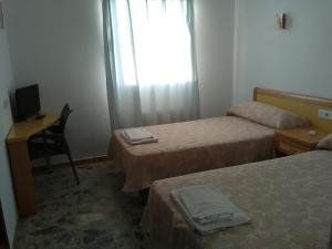 a room with two beds and a desk and a window at Hostal Restaurante el Cazador in Nuévalos