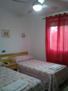 a room with two beds and a window with red curtains at Hostal Restaurante el Cazador in Nuévalos