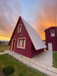 una casa roja con una puesta de sol en el fondo en Cabañas del Rosario en Puerto Santa Cruz