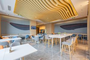 a restaurant with white tables and chairs and a yellow ceiling at Holiday Inn Express Huludao Seaview, an IHG Hotel in Huludao