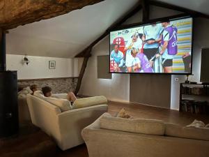 zwei Personen sitzen auf Sofas in einem Wohnzimmer mit einem Fernseher in der Unterkunft Country Villa for 18 Pool Cinema Football Pitch in Verteillac
