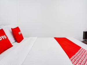 ein weißes Bett mit roten Kissen und einem TV in der Unterkunft OYO 91544 Homestay Biru Blukid in Sidoarjo