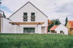 a white house with a wooden roof and green grass at Kardamom Studio Apartman in Szigliget