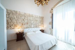 une chambre avec un lit blanc et un mur en pierre dans l'établissement Syracusia, à Syracuse