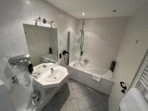a white bathroom with a sink and a bath tub at Hotel Am Tiergarten in Nürburg
