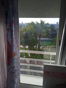 a window with a view of a beach and palm trees at Sidi Rahal Villa avec piscine à 5min de la plage in Dar Hamida